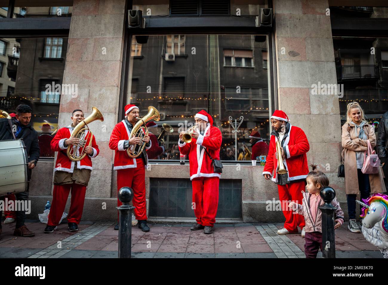 Imagen de un grupo de romaníes tocando música y cantando para preparar su actuación para una navidad en las calles de Belgrado, vestidos de papá noel. Foto de stock