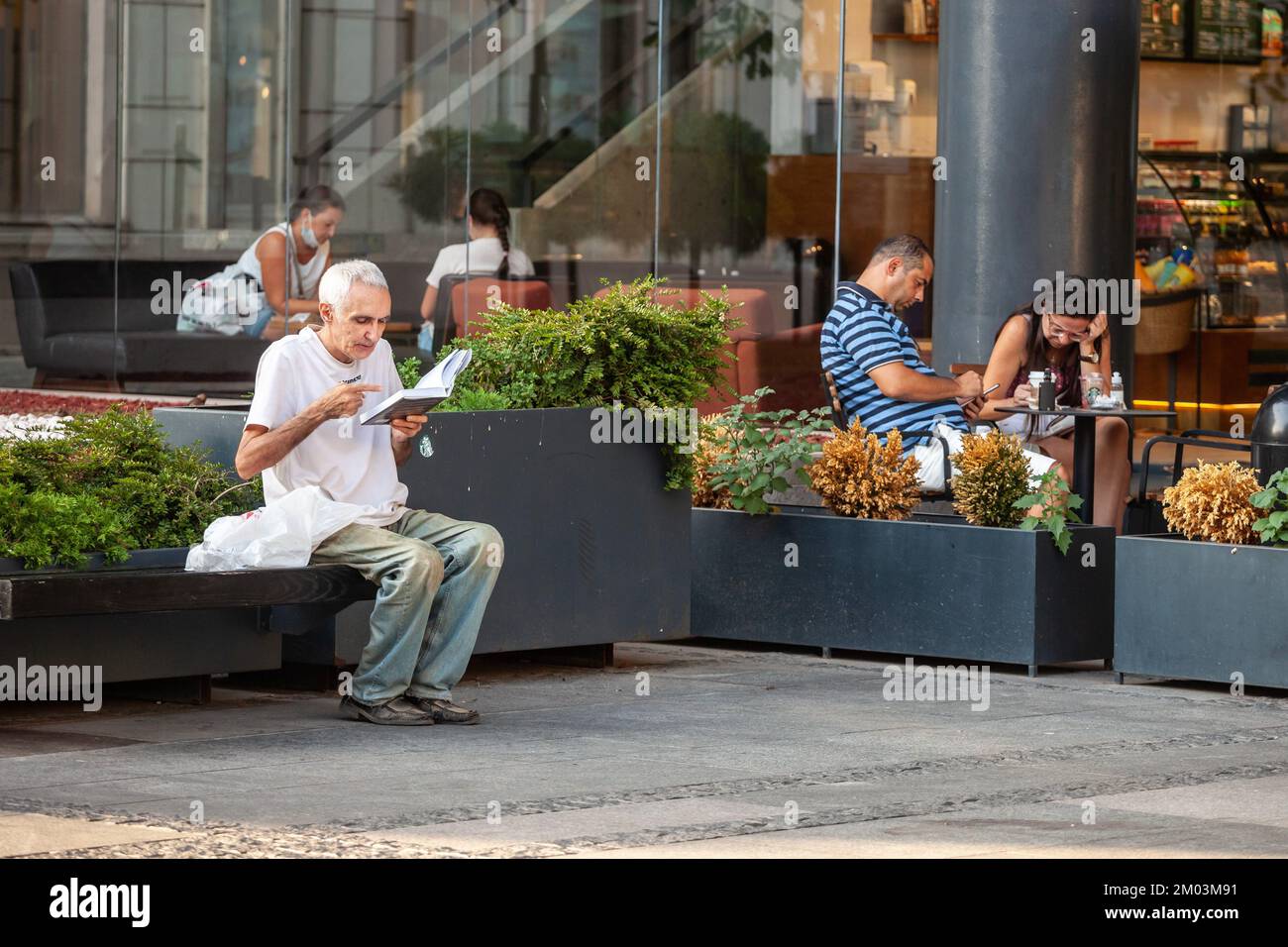 Imagen de un anciano sentado en un banco público leyendo un libro al aire libre en Belgrado, la ciudad más grande de Serbia. Foto de stock