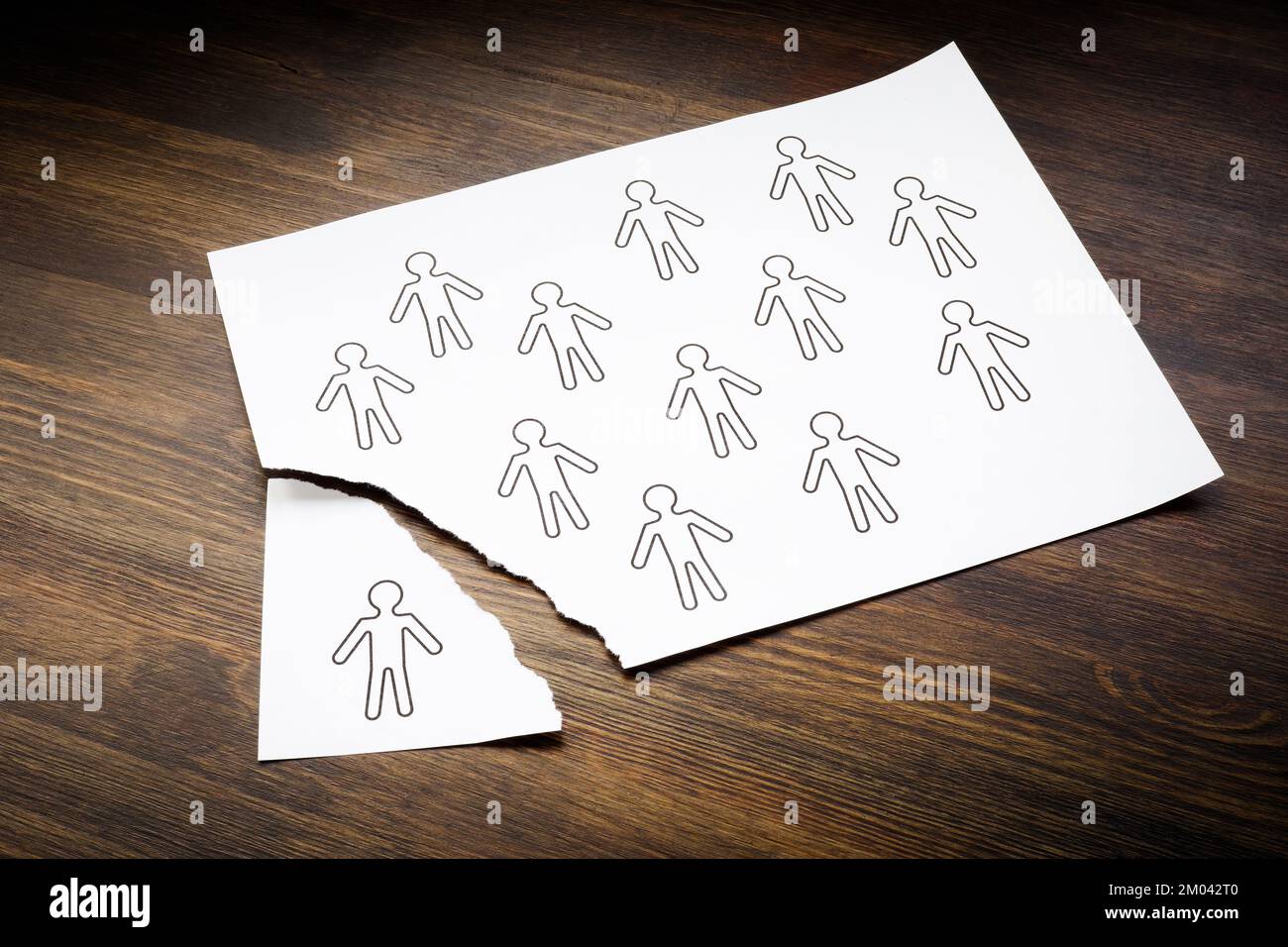 Concepto de empleados desvinculados. Figuras de personas en una hoja de papel y una es arrancada. Foto de stock