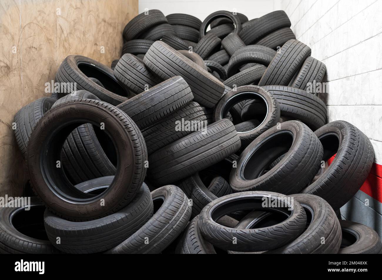 Pila de neumáticos negros viejos del vehículo apilados en la habitación pequeña del almacén de la disposición Foto de stock