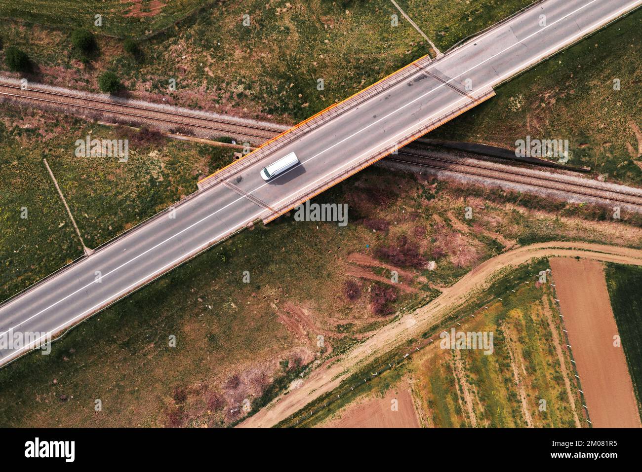 Camioneta blanca cruzando el paso elevado del ferrocarril en una autopista vacía, vista aérea de arriba abajo de la imagen del punto de vista del drone para el concepto de transporte y de negocio de la entrega Foto de stock