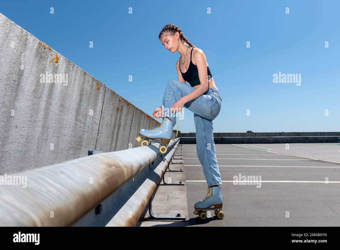 Chica amarrando sus patines, fondo urbano. Preparación para el patinaje sobre ruedas. Foto de stock
