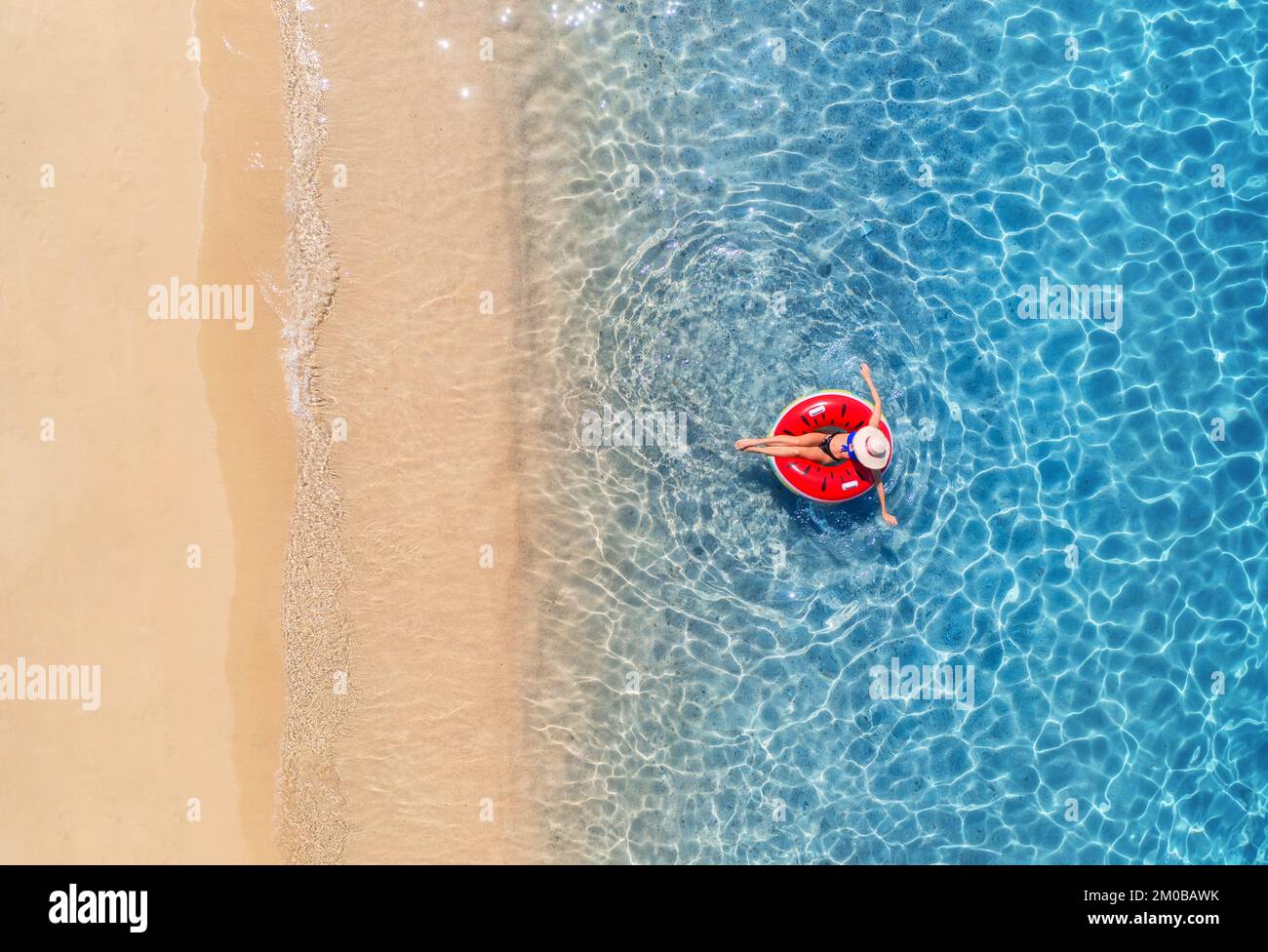 Vista aérea de una mujer en sombrero nadando con anillo rojo en el mar azul al amanecer en verano. Paisaje tropical con chica, agua clara, olas, arena be Foto de stock