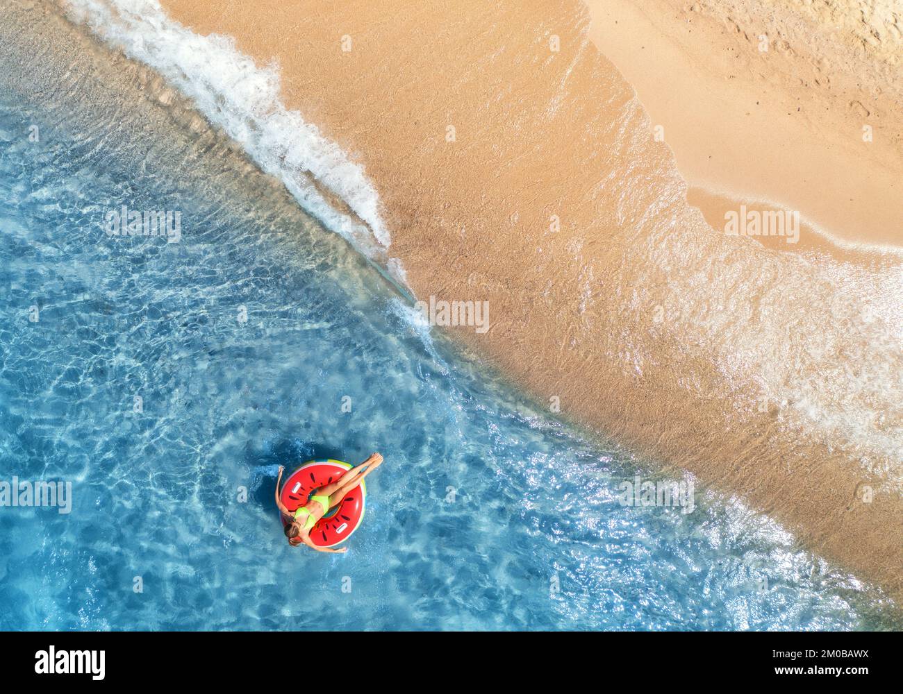 Vista aérea de una joven nadando con un anillo rojo en el mar azul con olas al atardecer en verano. Paisaje tropical con niña, agua clara, arena Foto de stock