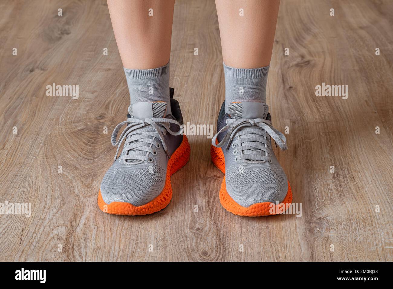Zapatillas grises y calcetines grises en los pies de la mujer. Pies de pie apoyados en sneakers de malla con suela naranja acanalada. Nuevas zapatillas para un estilo de vida activo. Foto de stock