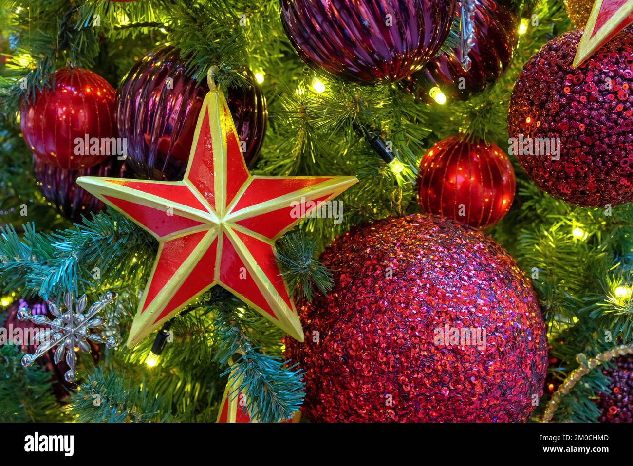 Estrella roja de cinco puntas con un borde dorado en el árbol de Navidad con guirnaldas. Foto de stock