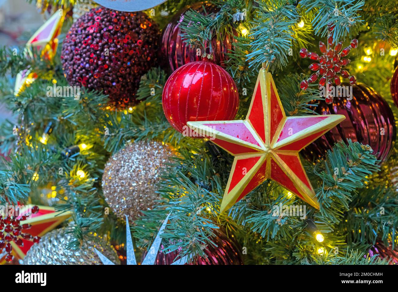 Estrella roja de cinco puntas con un borde dorado en el árbol de Navidad con guirnaldas. Foto de stock