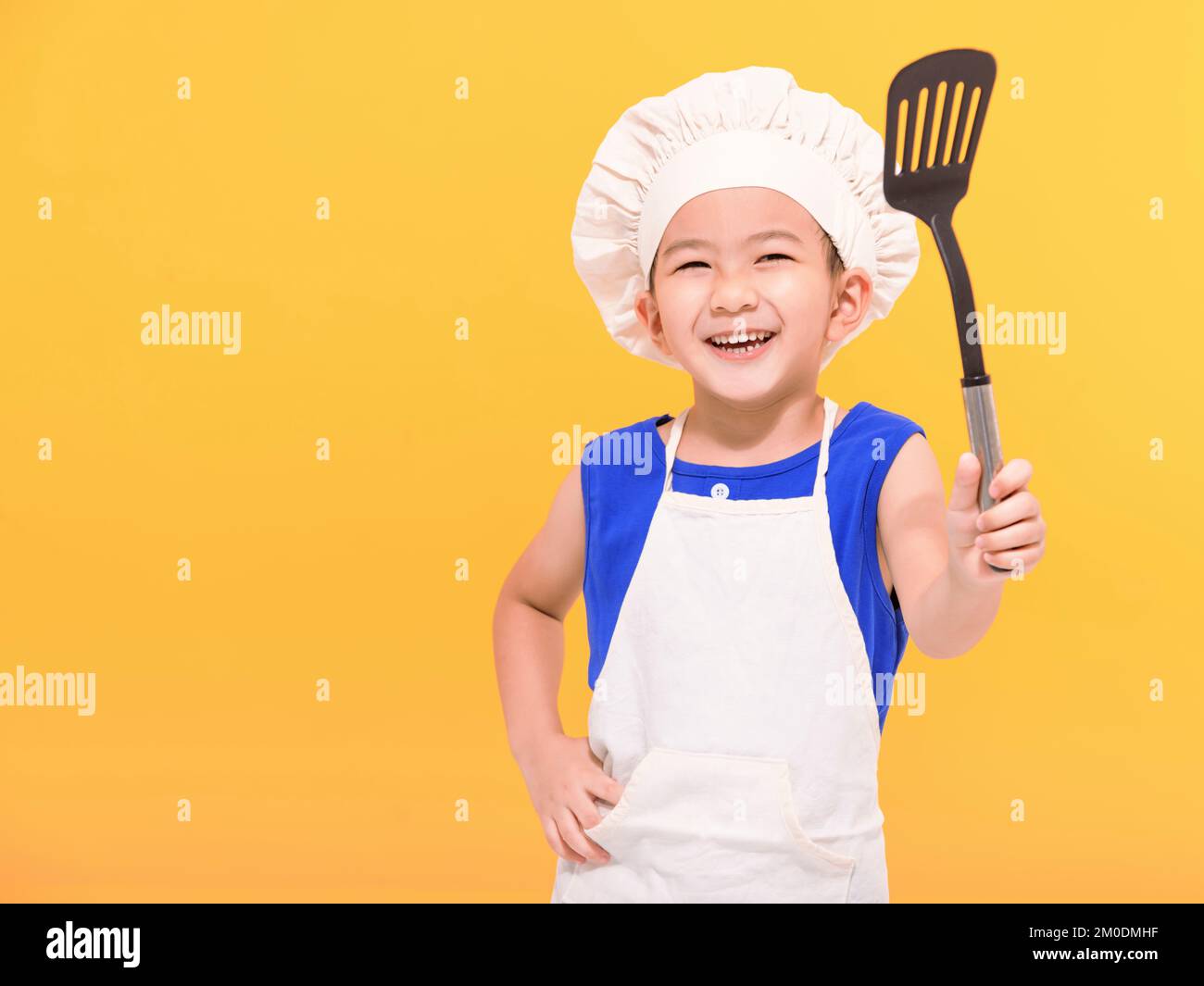 Niño caucásico jugando a chef, niño en delantal y gorro de cocinero  emocionalmente posando sobre fondo amarillo