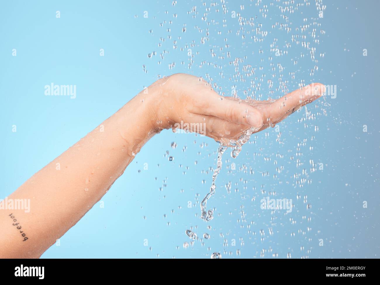 Agua, ducha de mano y limpieza para el cuerpo, el bienestar y el cuidado de la piel, salpicaduras e higiene con hidratación sobre el fondo azul del estudio. Cuidado de la piel, del cuerpo Foto de stock