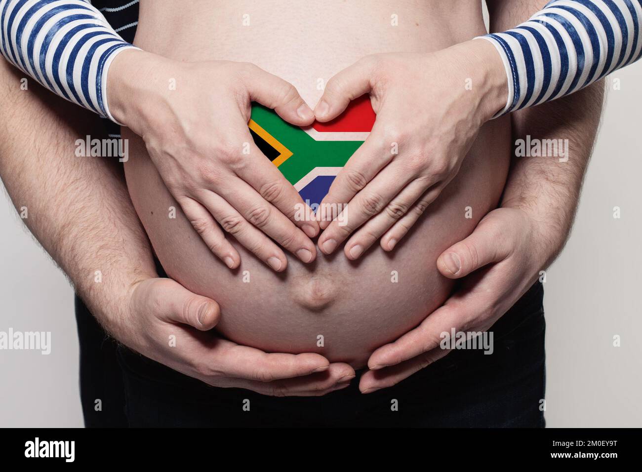 Hombre abrazando a mujer embarazada vientre y corazón con bandera de República de Sudáfrica colores primer plano Foto de stock