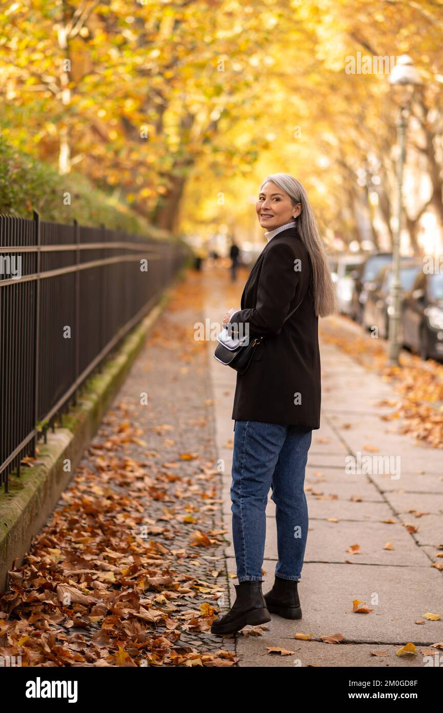 Mujer madura de pelo largo y buen aspecto en la calle del parque de otoño Foto de stock