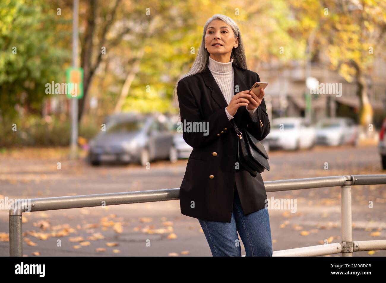 Mujer de pelo largo con un abrigo negro esperando a alguien en la calle Foto de stock