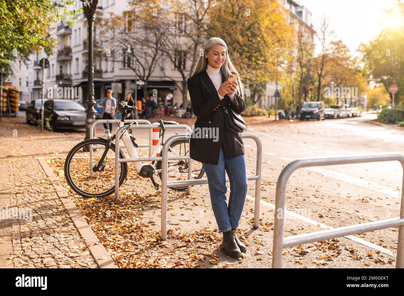 Mujer de mediana edad de pelo largo con un teléfono en la mano cerca de las bicicletas Foto de stock
