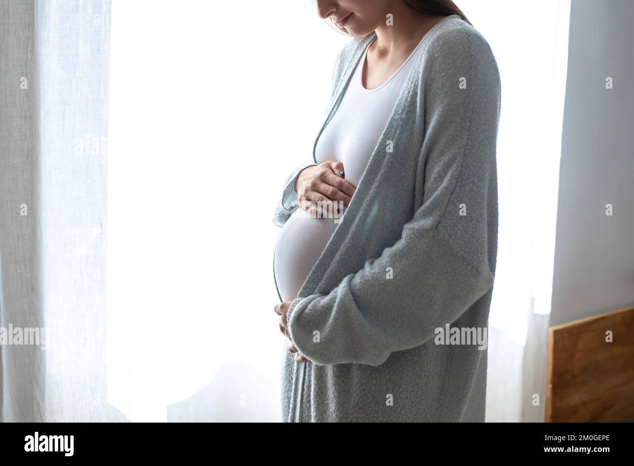 Mujer joven embarazada con el vientre grande en la ventana de la casa Foto de stock