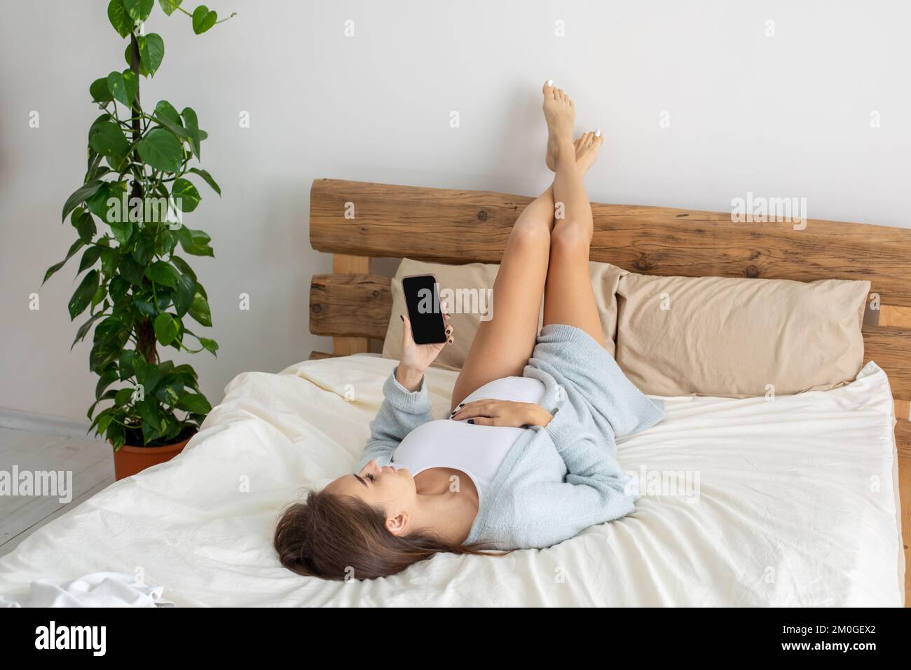 Mujer joven embarazada tumbada en la cama con las piernas levantadas y navegando por Internet Foto de stock