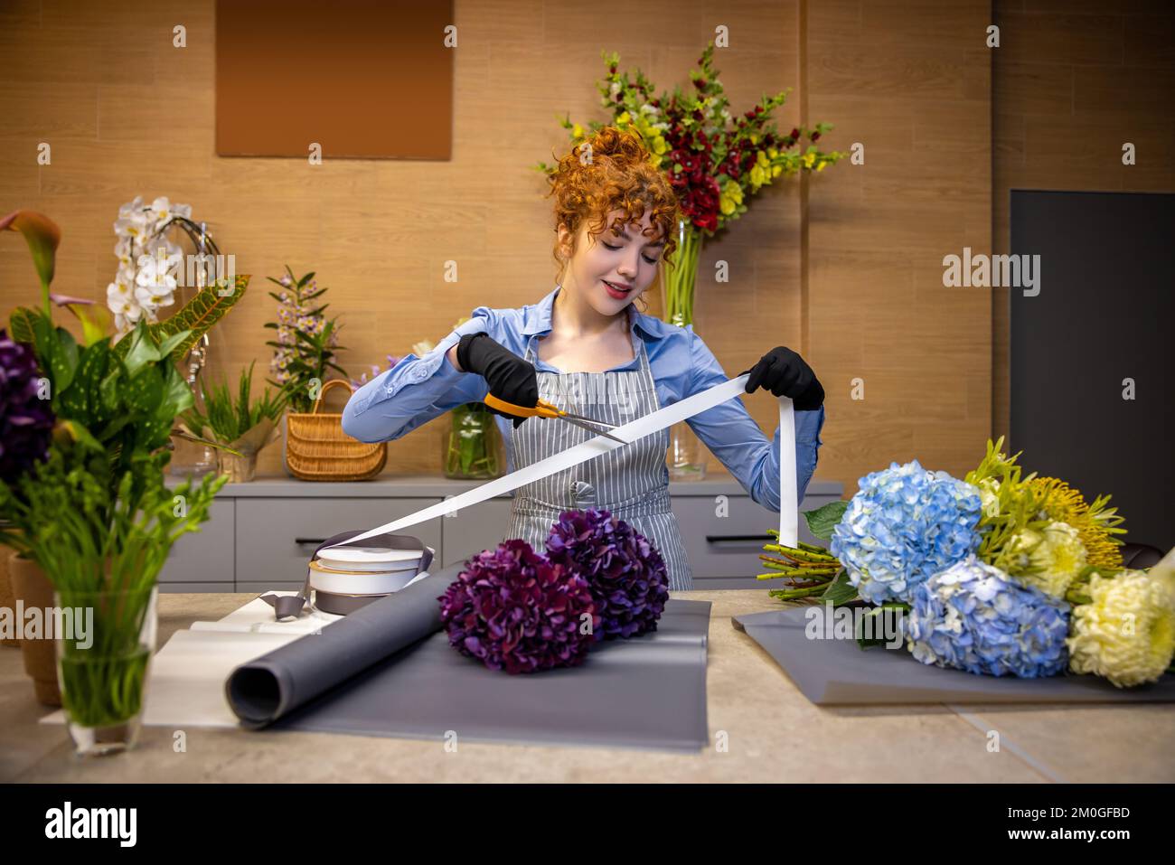 Florista de jengibre lindo buscando involucrados mientras se hace una cubierta para el bouquet Foto de stock