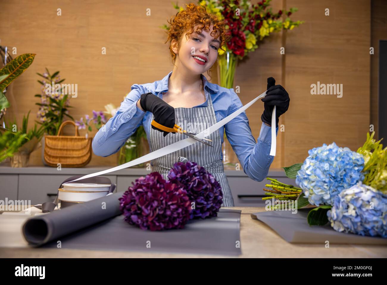 Florista de jengibre lindo buscando involucrados mientras se hace una cubierta para el bouquet Foto de stock