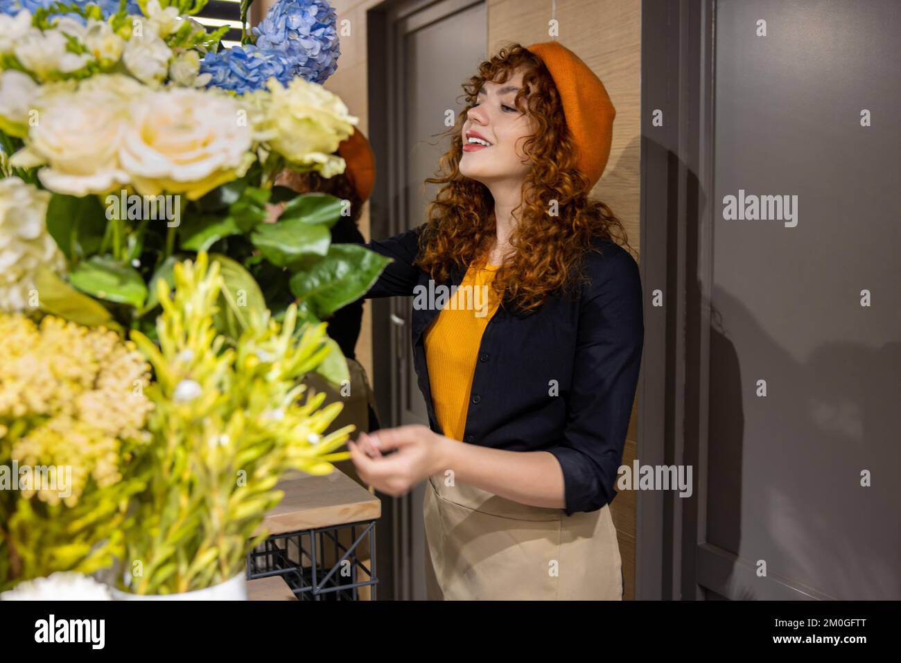 Chica bonita en una boina naranja en una floristería Foto de stock
