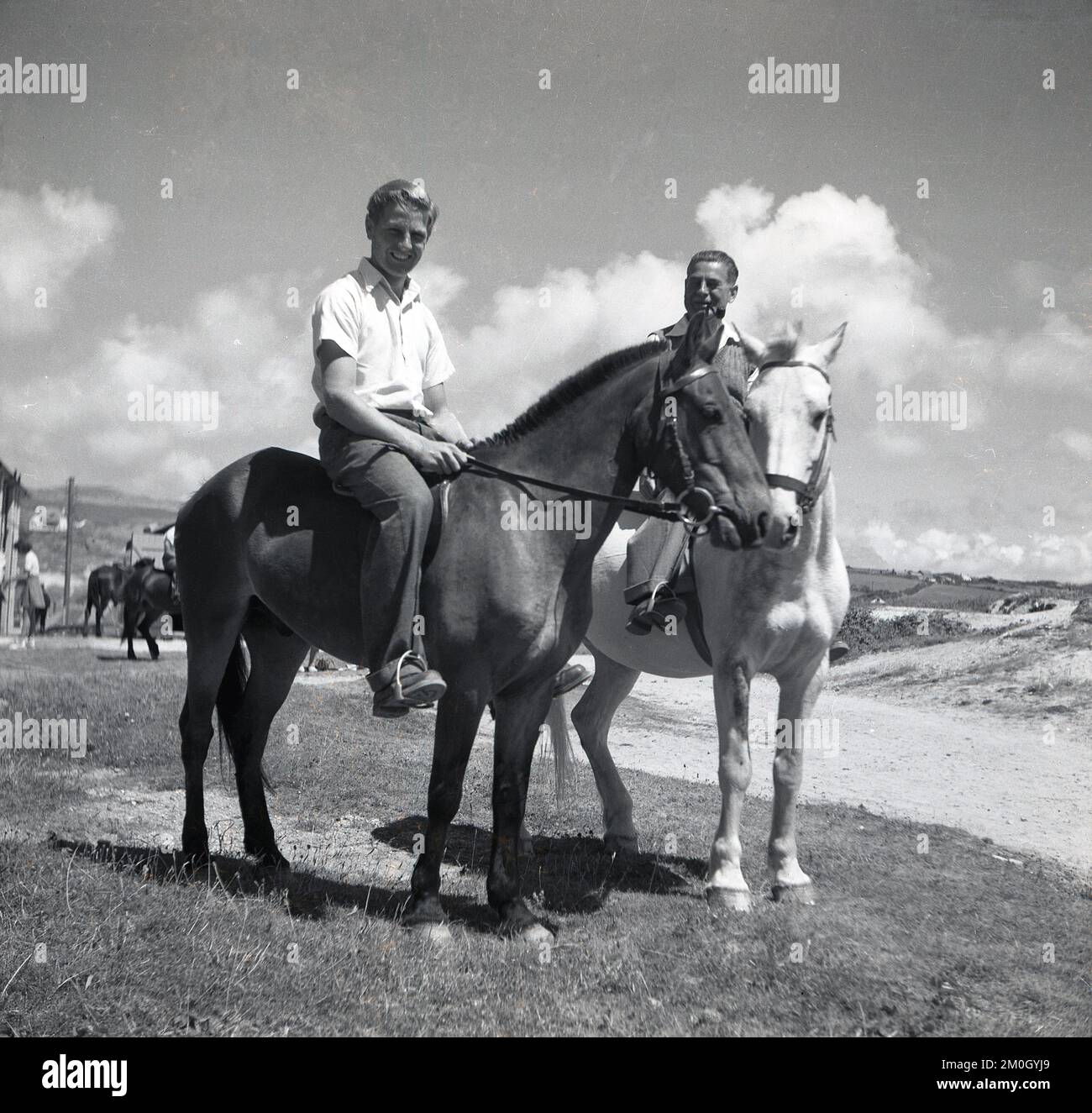 1950s, histórico, paseo de vacaciones, dos hombres a caballo en un terreno arenoso, césped en una costa, Inglaterra, Reino Unido. Foto de stock
