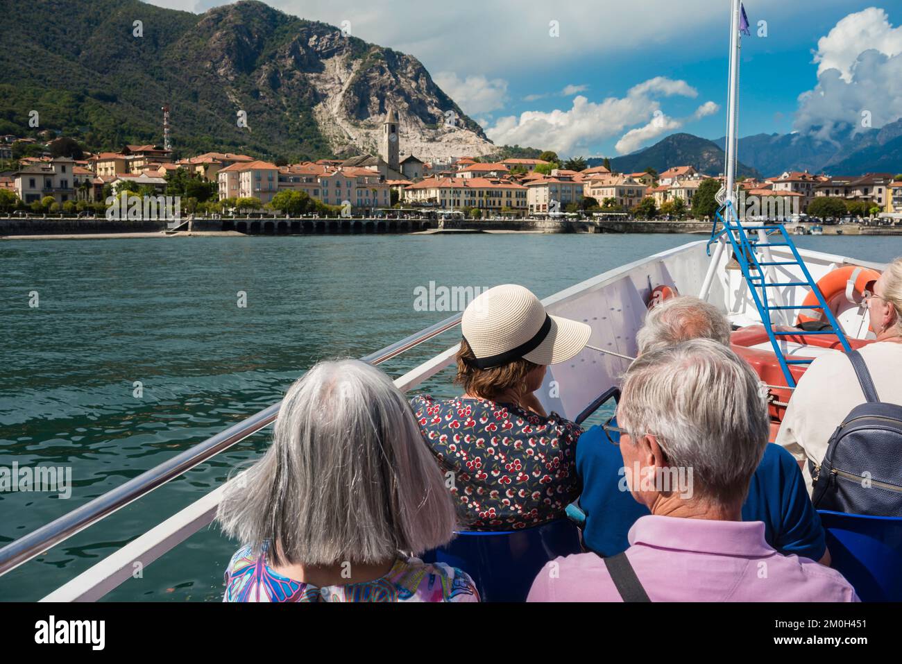 Italia Turismo de los lagos, vista trasera En verano de los pasajeros maduros a bordo de un ferry en el Lago Maggiore acercándose a la ciudad a orillas del lago de Baveno, Piamonte, Italia Foto de stock