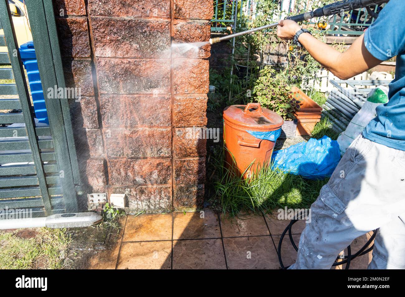Trabajador que usa pistola de chorro de agua a alta presión para lavar y limpiar la pared sucia con musgo en renovación Foto de stock
