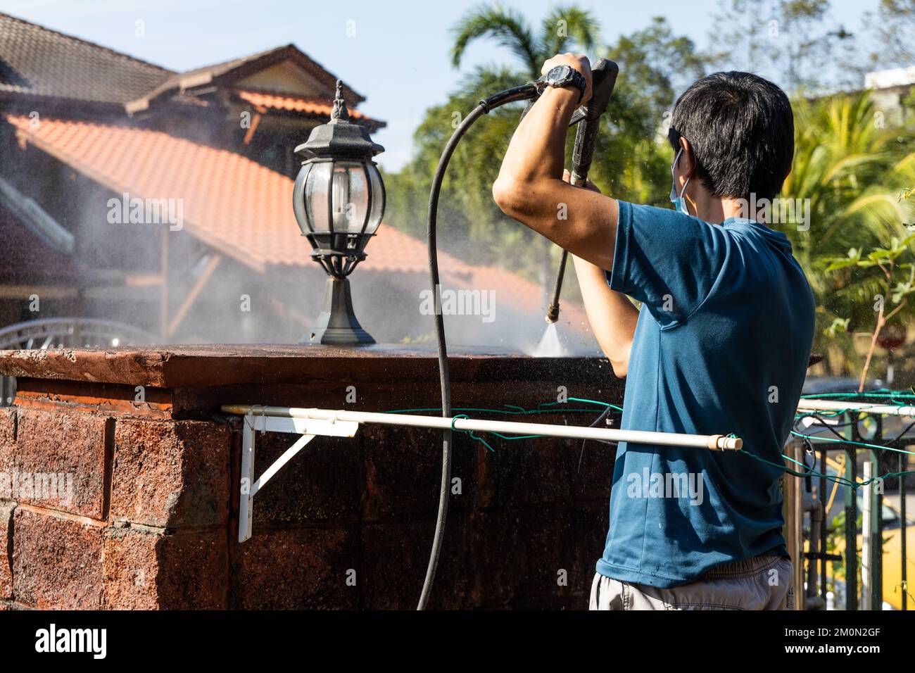 Trabajador que usa pistola de chorro de agua a alta presión para lavar y limpiar la pared sucia con musgo en renovación Foto de stock