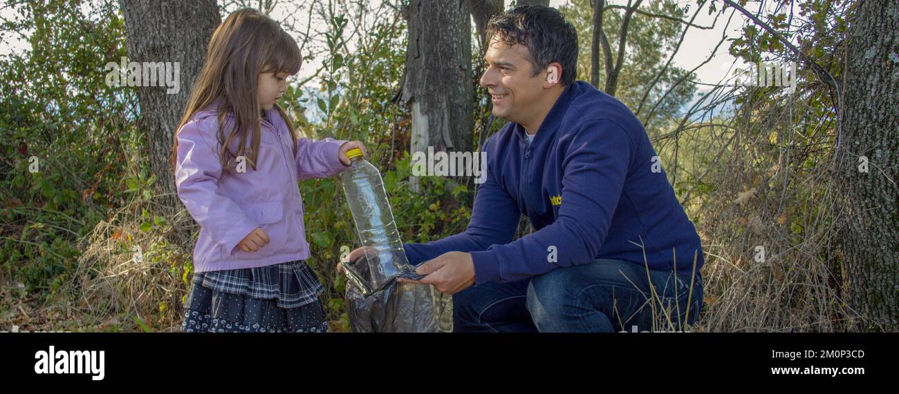Imagen de un padre y una hija sonrientes mientras limpian un bosque de basura y botellas de plástico. Familia respetuosa con el medio ambiente y reciclaje. Foto de stock