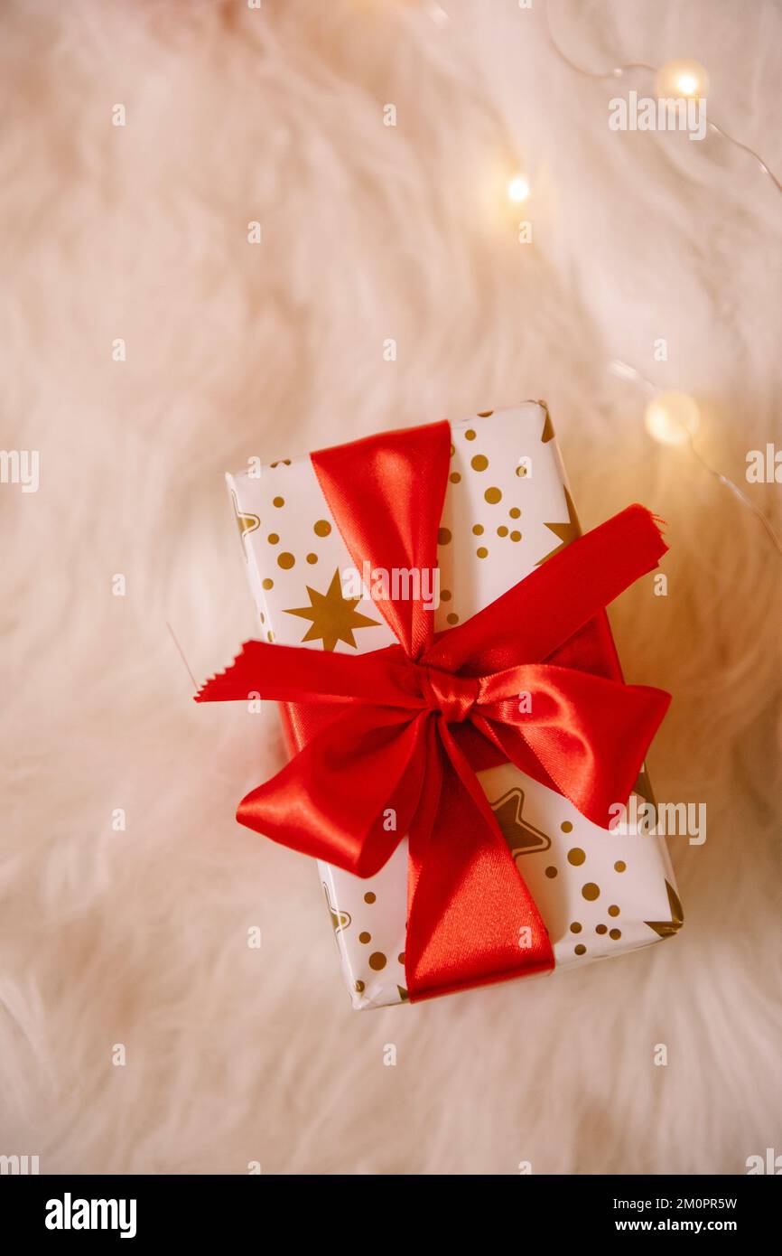 Una vista superior de una caja de regalo de Navidad con un lazo rojo sobre la tela suave decorada con luces Foto de stock