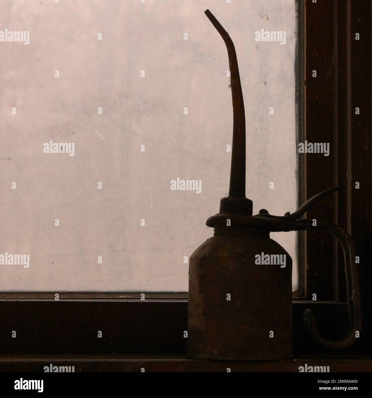 Bodegón: El still atemporal de un aceite rústico vintage puede bañarse en la suciedad y la pátina en el descanso en el umbral de una ventana de taller cubierta de tierra. Foto de stock