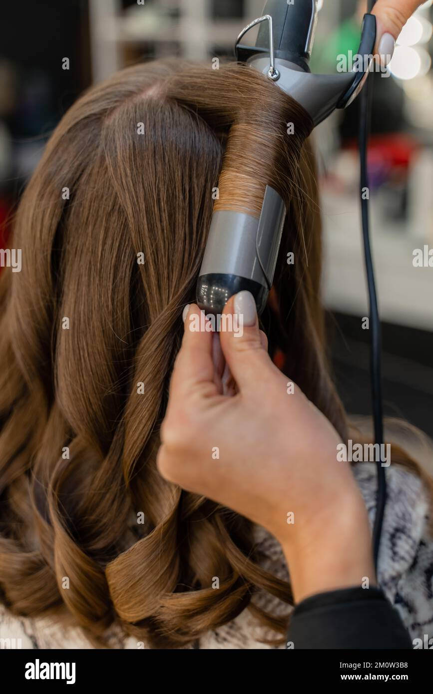 El peluquero prepara a una mujer, hace un peinado con rizos utilizando un  rizador. Pelo largo natural marrón claro. Concepto de autocuidado  Fotografía de stock - Alamy