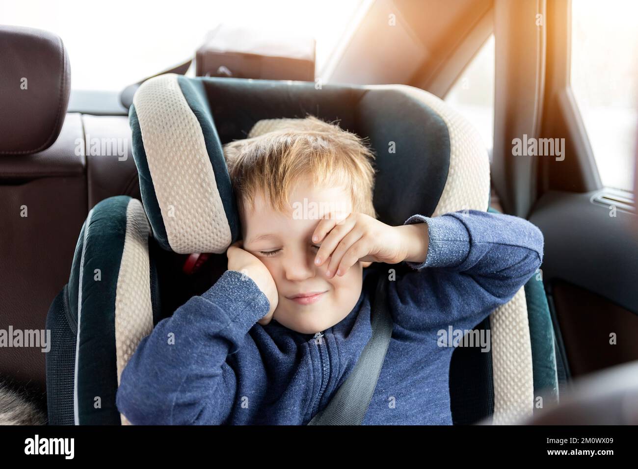 Lindo niño caucásico despertar y frotar los ojos en el asiento de seguridad infantil en el coche durante el viaje por carretera. Adorable bebé soñando dormido silla cómoda durante Foto de stock