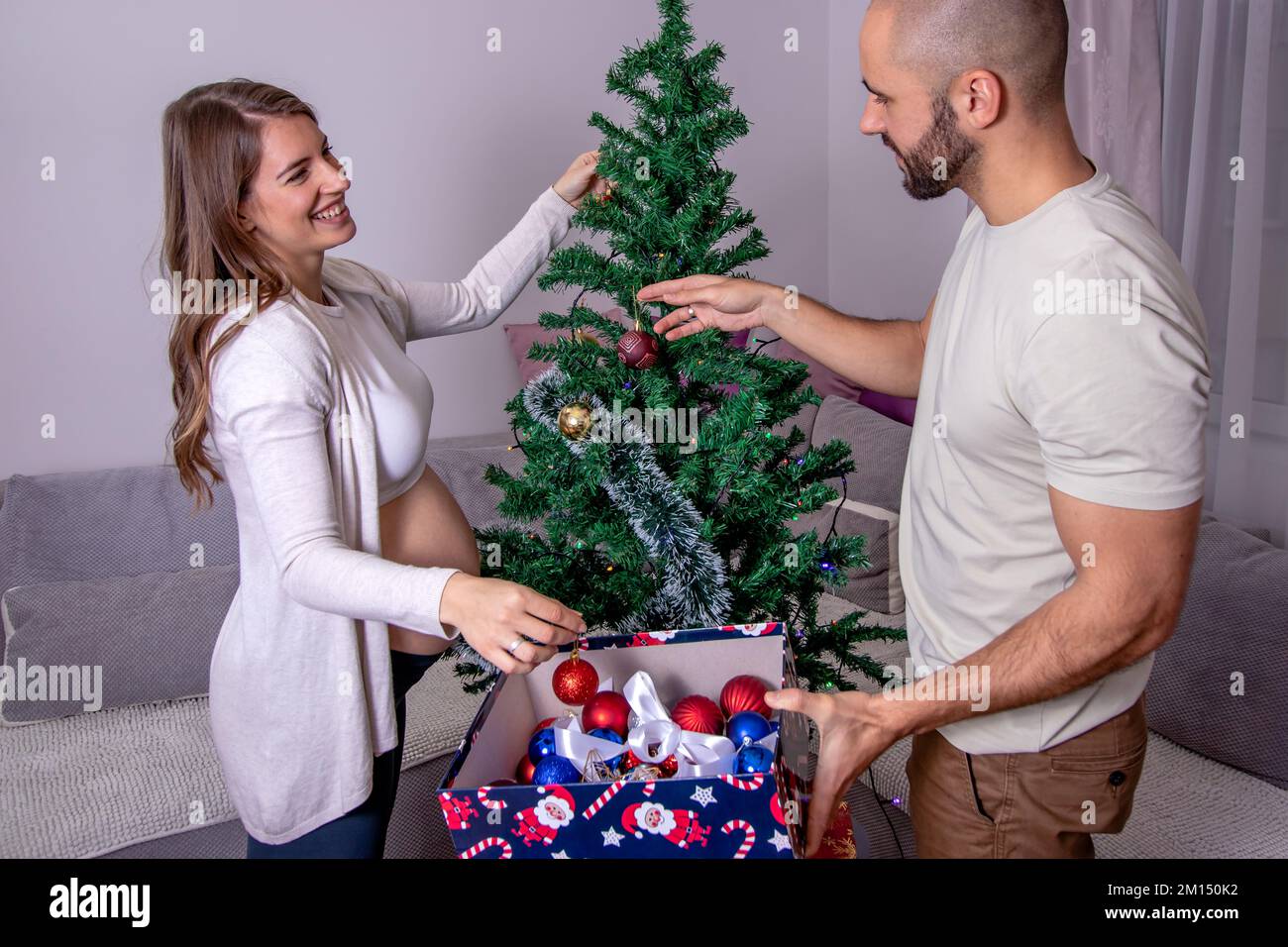 Mujer embarazada con su pareja decorando el árbol de Navidad. Una joven  pareja amorosa que se prepara para el parto. Mejor regalo de Navidad  Fotografía de stock - Alamy