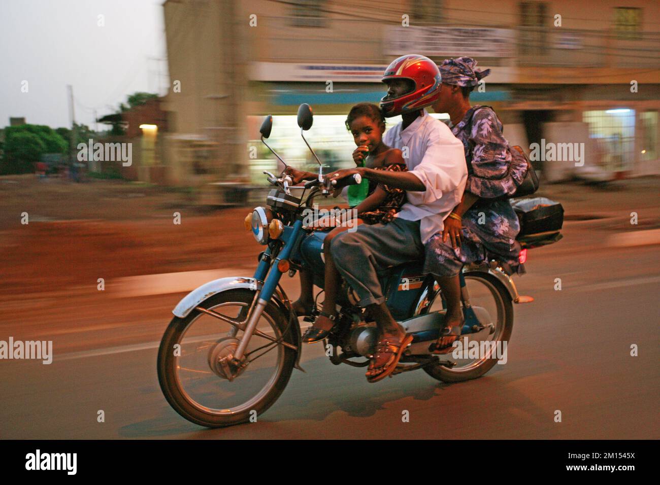 El hombre monta su motocicleta con su hijo y esposa en las calles de Bamako, la capital de Malí. Foto de stock