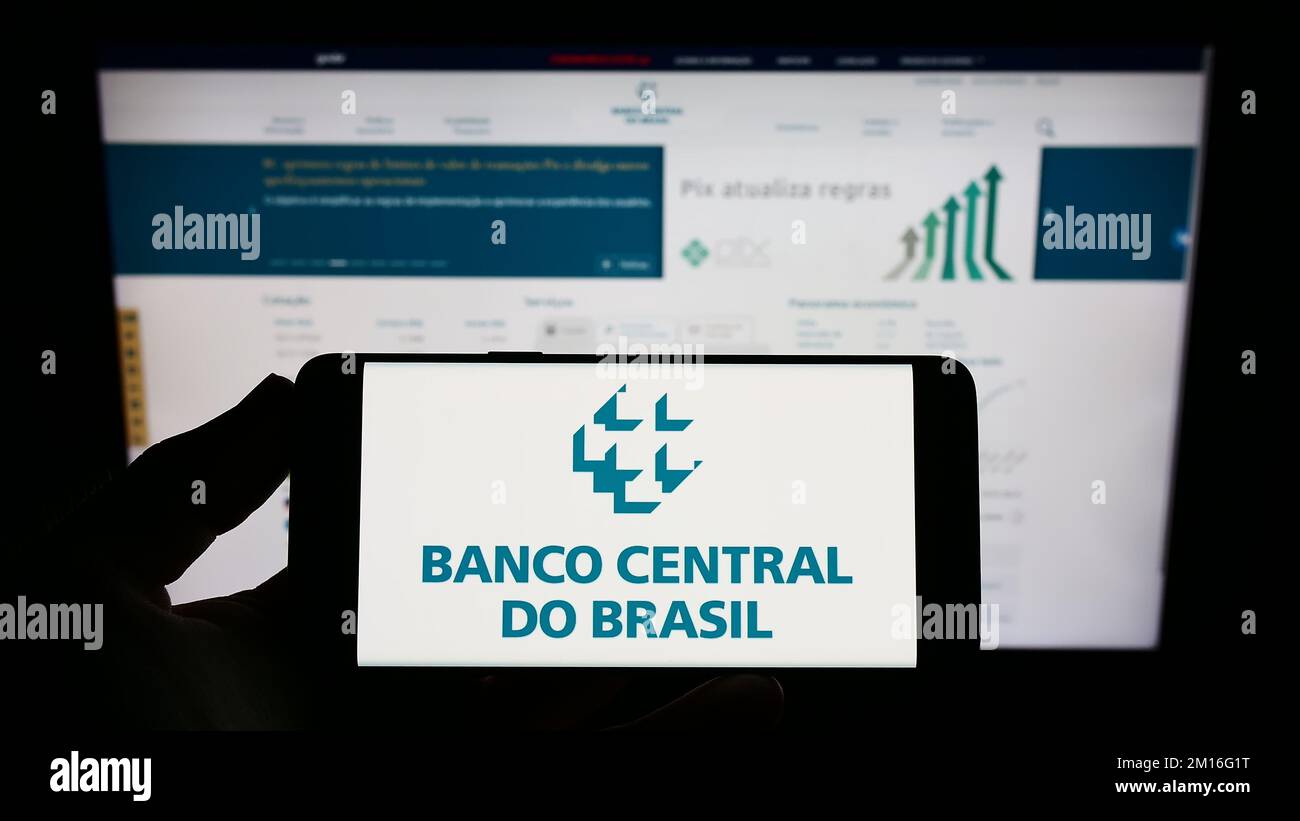 Persona que posee un smartphone con el logotipo del banco central Banco Central do Brasil (BCB) en la pantalla frente al sitio web. Enfoque la pantalla del teléfono. Foto de stock