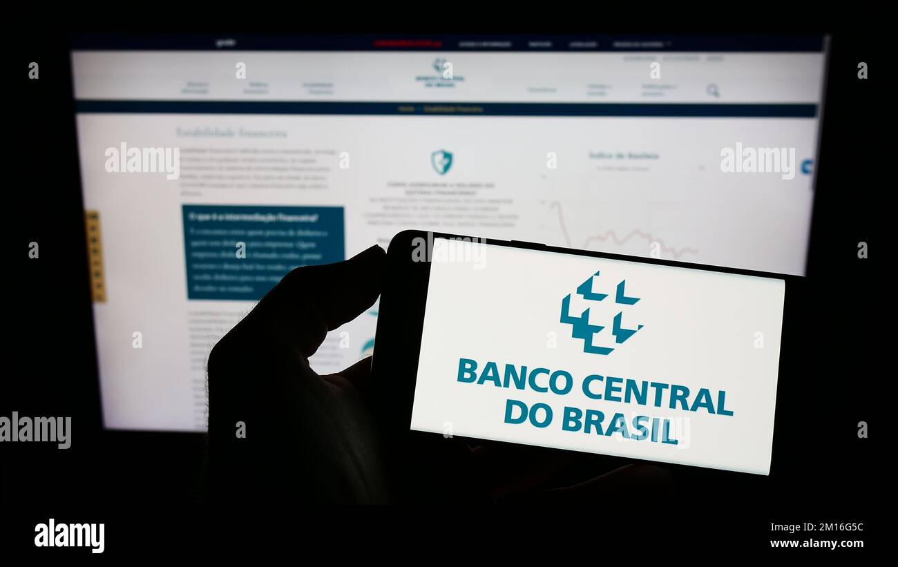 Persona que posee un celular con el logo del banco central Banco Central do Brasil (BCB) en la pantalla frente a la página web. Enfoque la pantalla del teléfono. Foto de stock