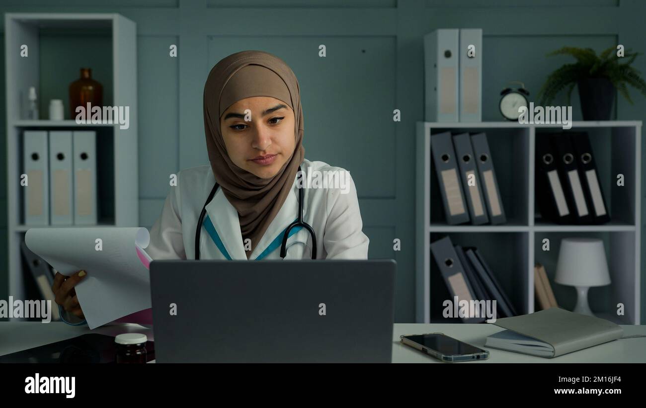 Joven médico árabe religión musulmana haciendo papeleo en la clínica hacer la investigación científica leer documentos de papel médico médico mujer seguro Foto de stock