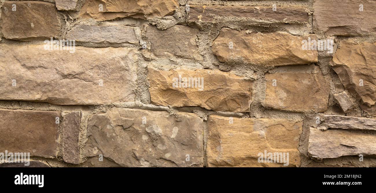 Resistente pared de piedra cortada en amarillo y beige, ideal para fondos, sin costuras alineadas Foto de stock