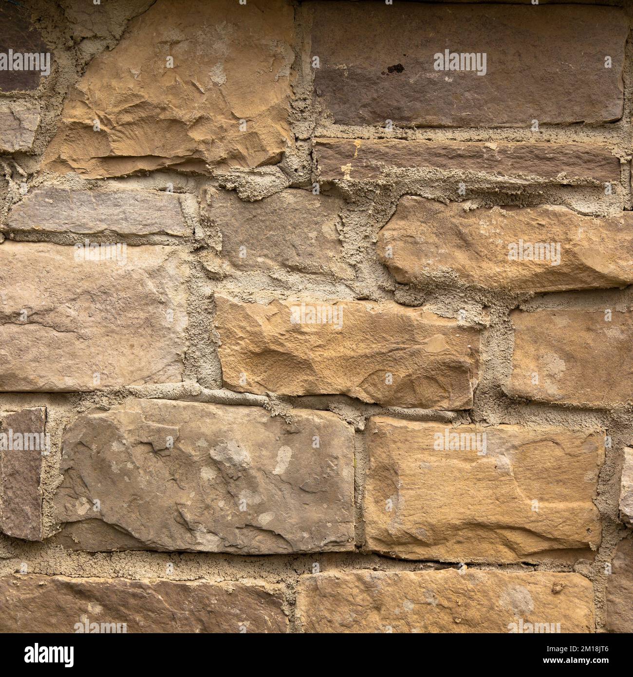 Resistente pared de piedra cortada en amarillo y beige, ideal para fondos, sin costuras alineadas Foto de stock