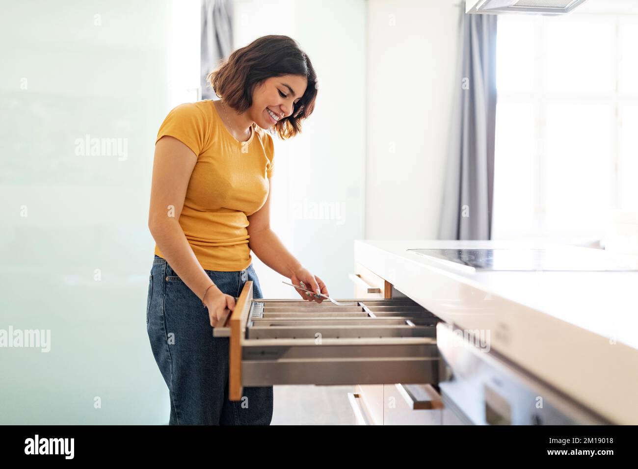 Joven mujer árabe arreglando los cubiertos en el cajón mientras limpia en la cocina Foto de stock