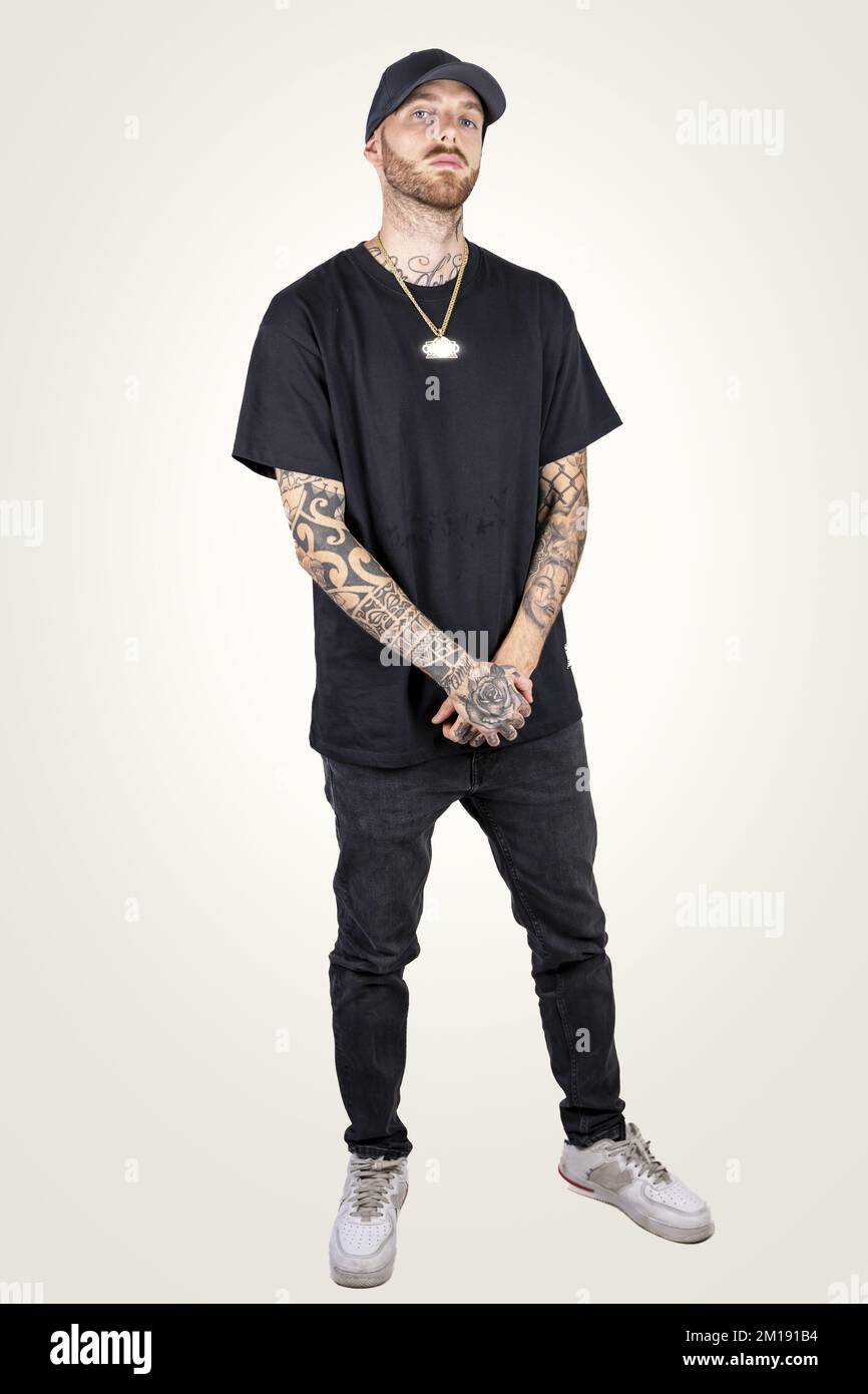 cantante de rap tatuado posando el estudio con ropa negra sobre un fondo blanco Fotografía de stock