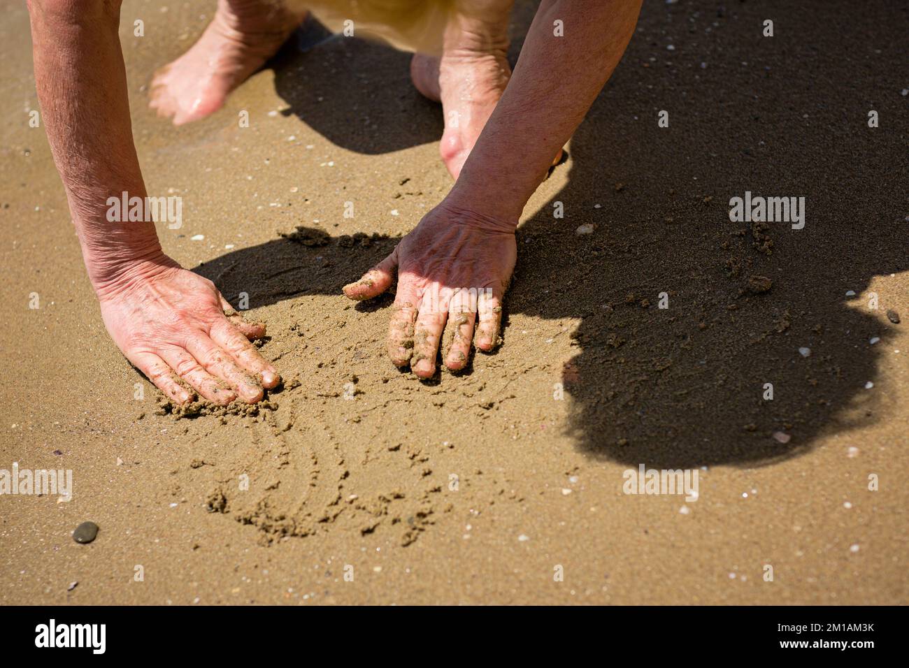 Mujer anciana irreconocible tocando la arena húmeda de la orilla del mar Foto de stock