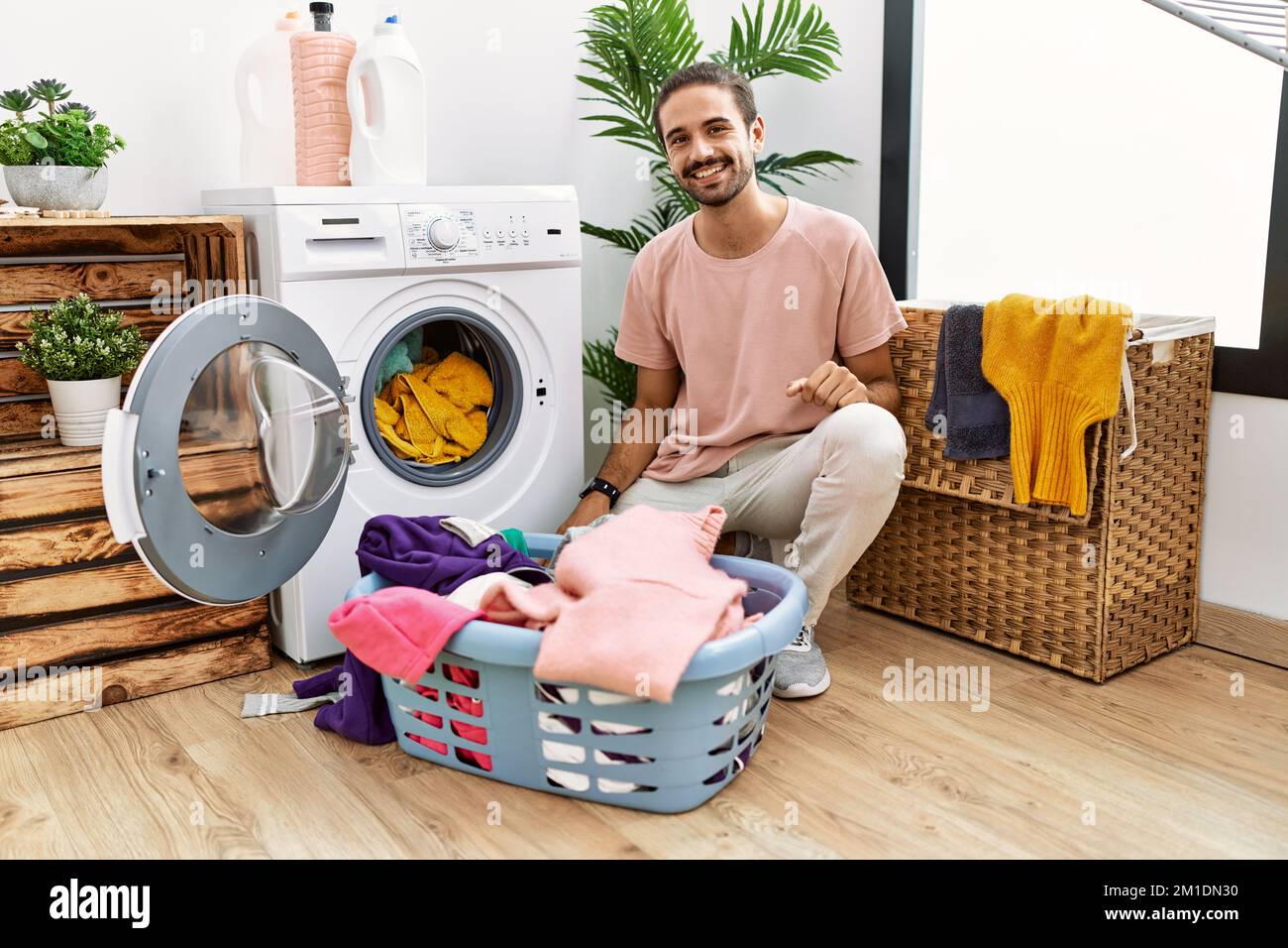 Joven hispano poniendo ropa sucia en la lavadora con un aspecto positivo y  feliz de pie y sonriendo con una sonrisa segura mostrando los dientes  Fotografía de stock - Alamy