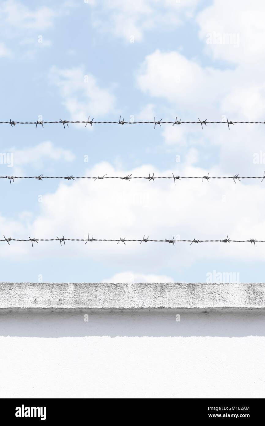 Alambre de púas Un tipo de alambre de acero construido con bordes afilados en la parte superior de una pared de prisión contra el cielo azul claro Foto de stock