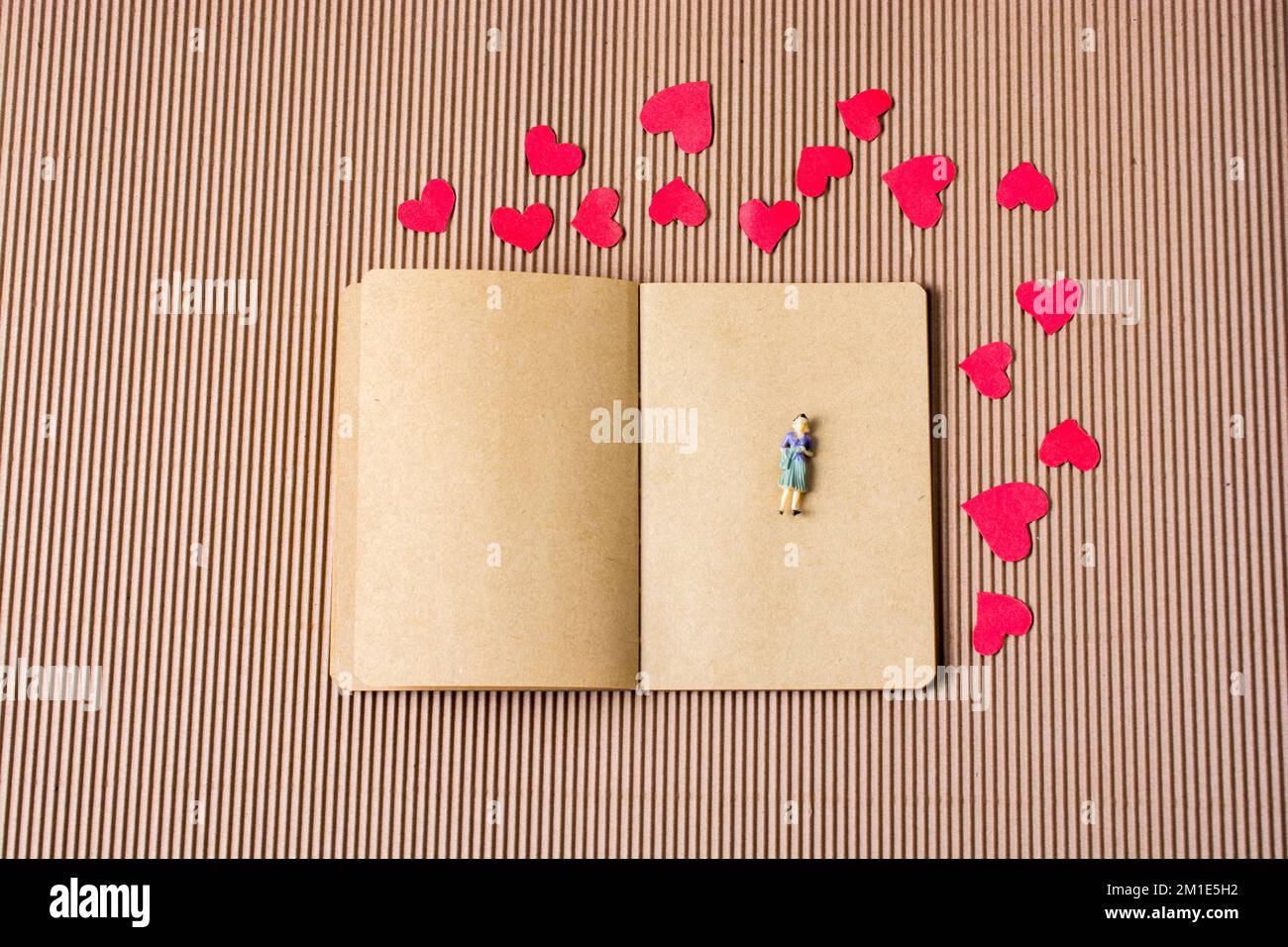 Figura de la mujer en el cuaderno con corazones de papel rojo alrededor Foto de stock