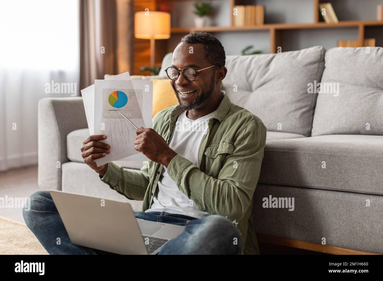 Feliz ocupado medio de edad negro masculino en gafas muestra gráficos, las tablas en webcam