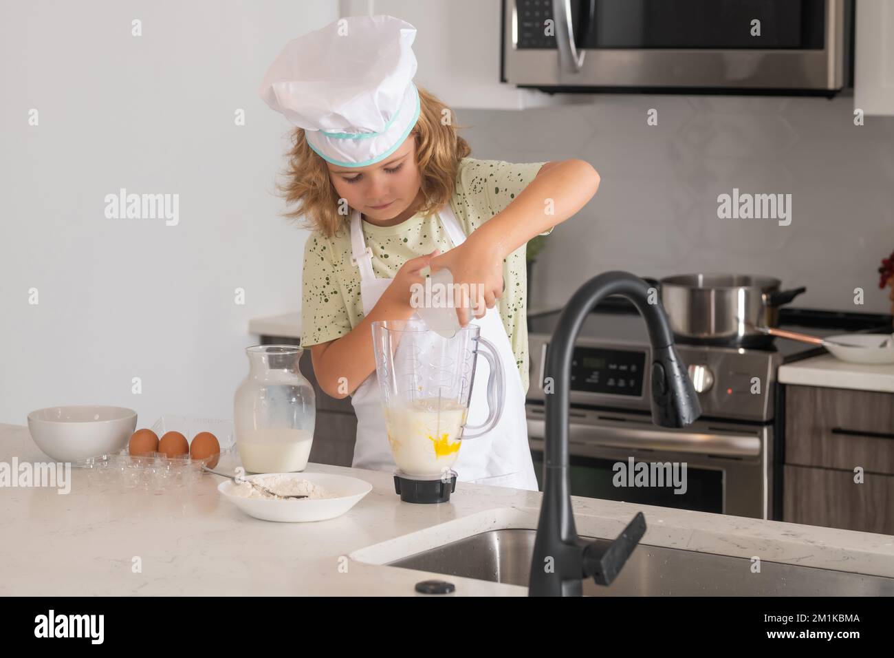 El cocinero del cocinero del cabrito está aprendiendo cómo hacer una torta en la cocina casera. Niño haciendo sabroso delicioso. Huevos, leche y harina Ingredientes para hornear galletas o. Foto de stock