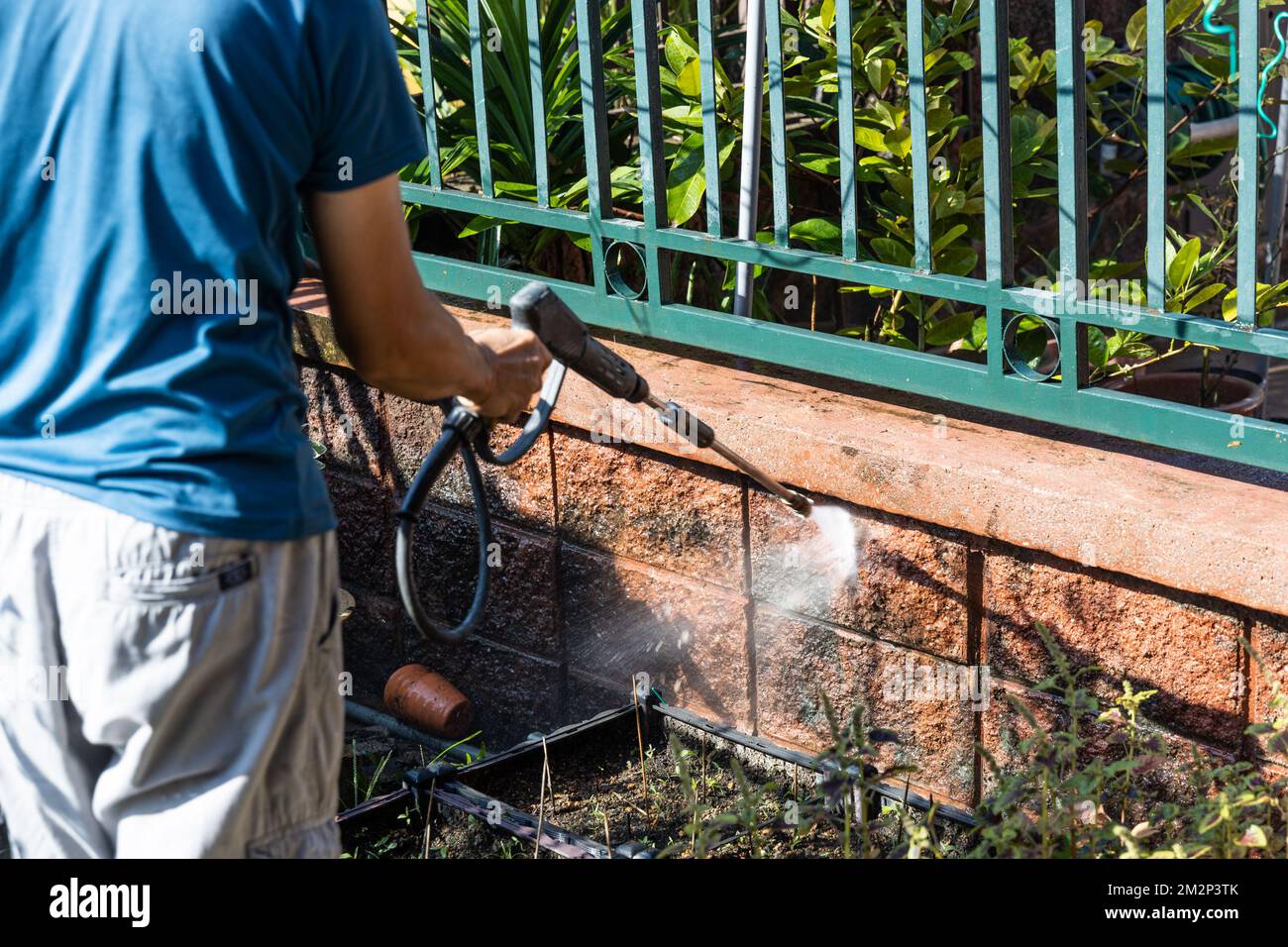Trabajador que usa pistola de chorro de agua a alta presión para lavar y limpiar la pared sucia con musgo en renovación Foto de stock