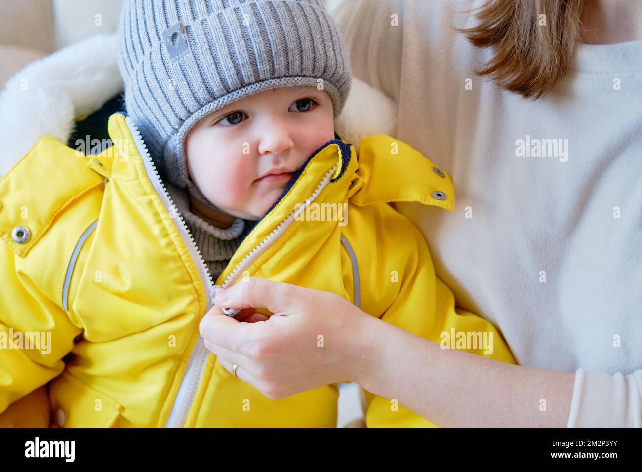 El niño está vestido con ropa cálida de invierno para un paseo al aire  libre. La madre de la mujer pone ropa en el niño pequeño del bebé para el  tiempo frío.