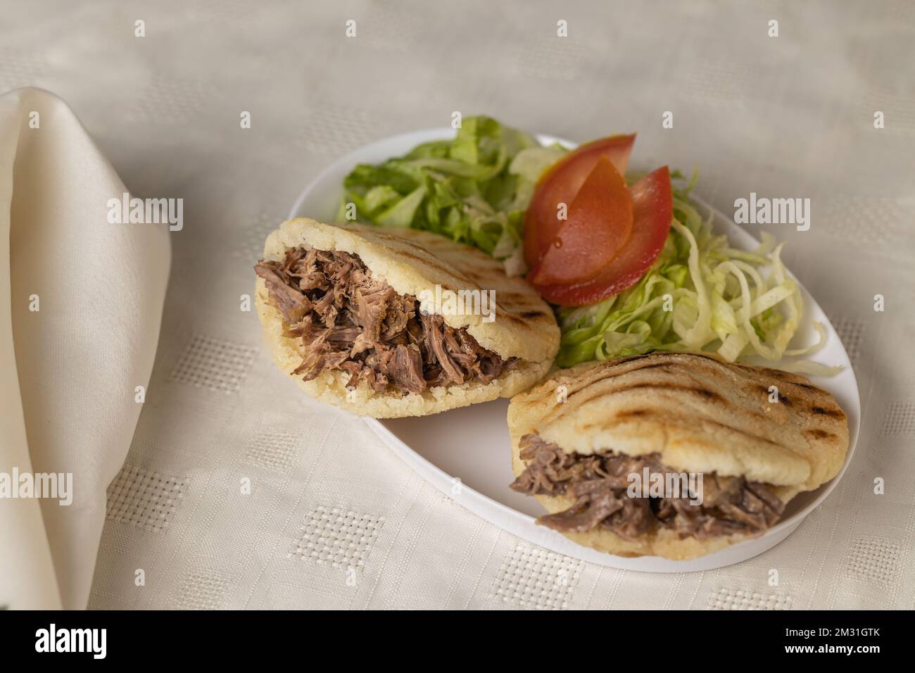 Arepas, comida típica venezolana, elaboradas con maíz y rellenas de carne rallada sobre mantel blanco. Foto de stock