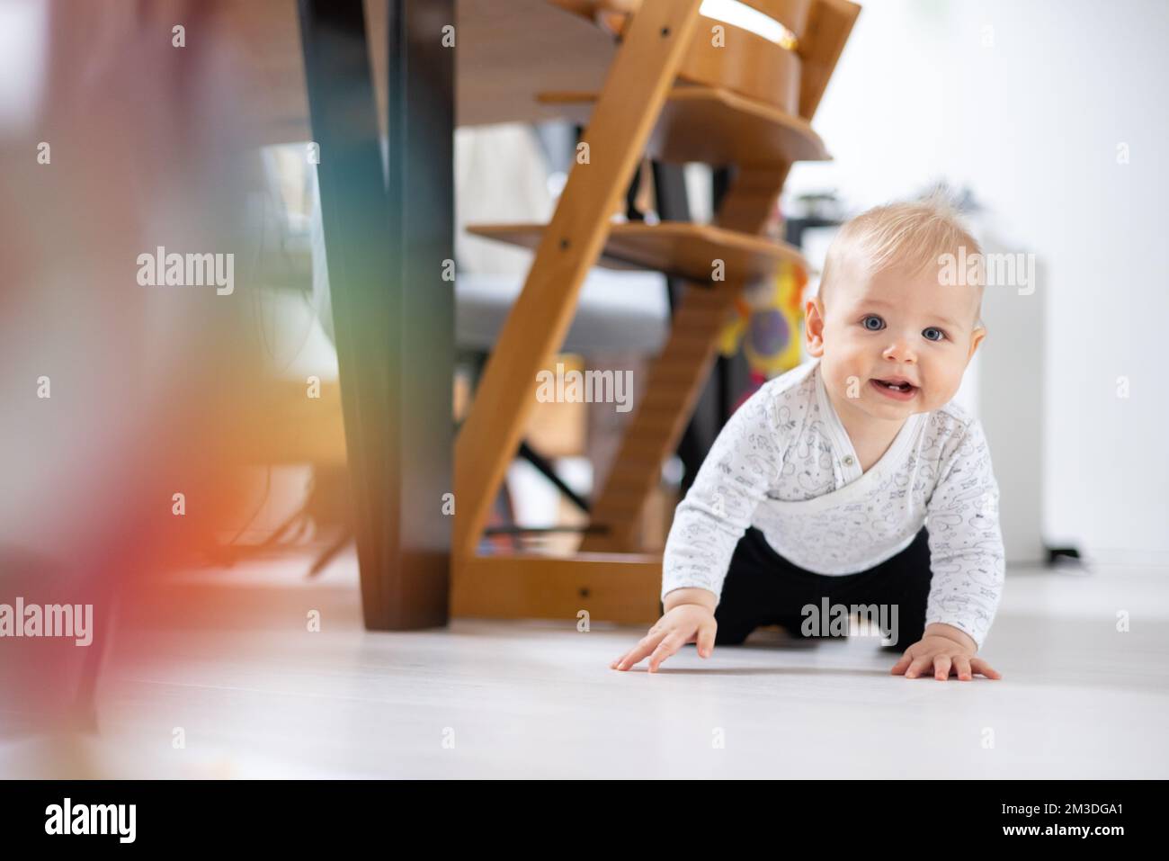 Lindo bebé niño gateando bajo la mesa del comedor en casa. Bebé jugando en casa. Foto de stock